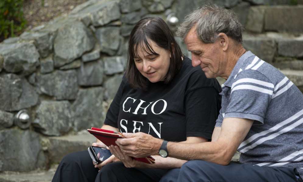 Woman and older man looking at a tablet together on some stone steps. 